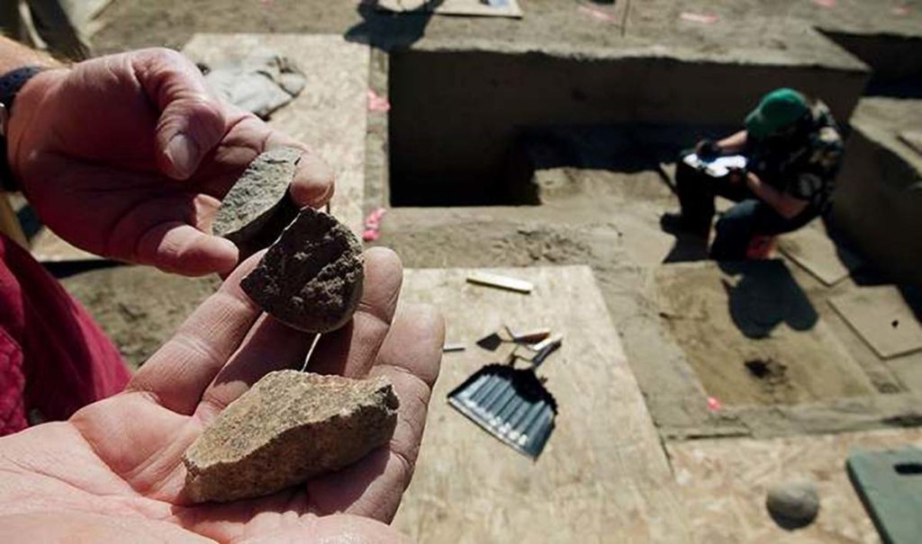 Close up photo of a worker's hands holding excavated materials. Another worker is working the background.