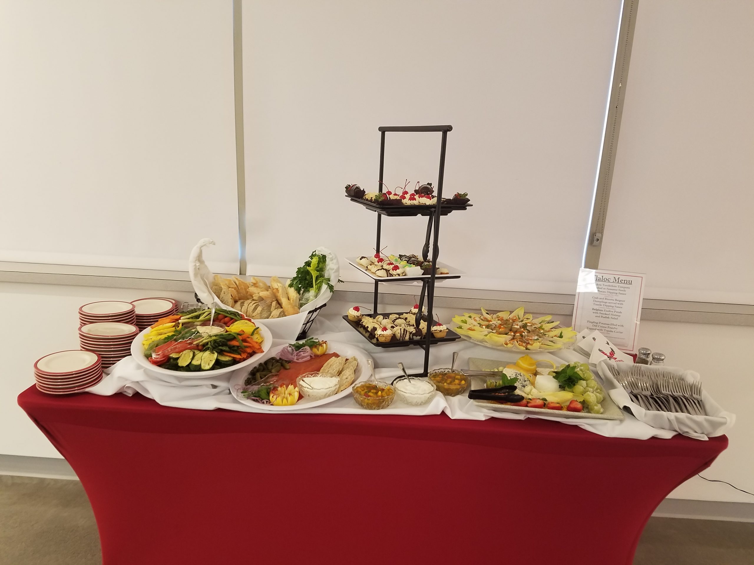 Photo of an example of EWU catering. It has various food such as vegetables and sweets. It is on a red table and includes plates and forks