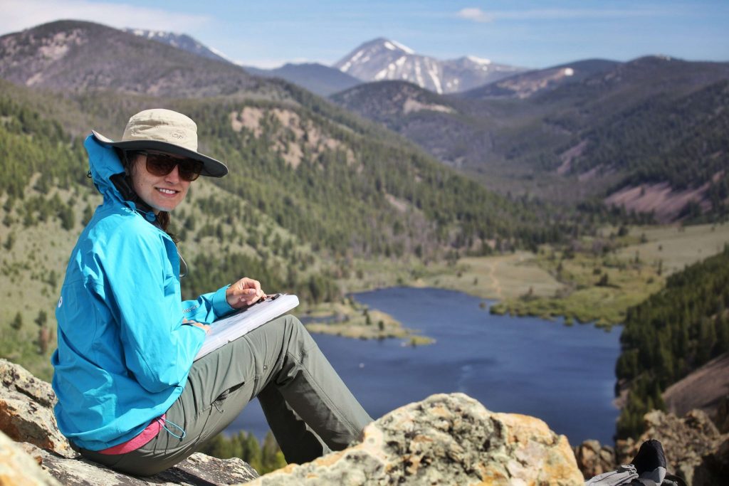 Student with notepad sitting above a valley with a lake