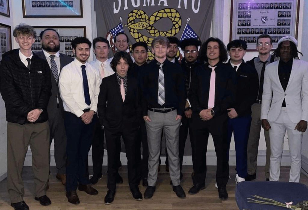 Group of fraternity students in formal wear in front of their fraternity banner