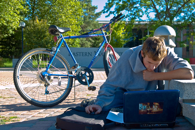 student in EWU campus mall sitting on the ground working on laptop next to a bike
