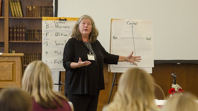Woman gesturing in front of two presentation boards. She is in front of a group of people