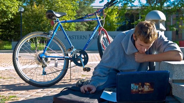 student sitting in the EWU campus mall. They are working on laptop and a bike is behind them